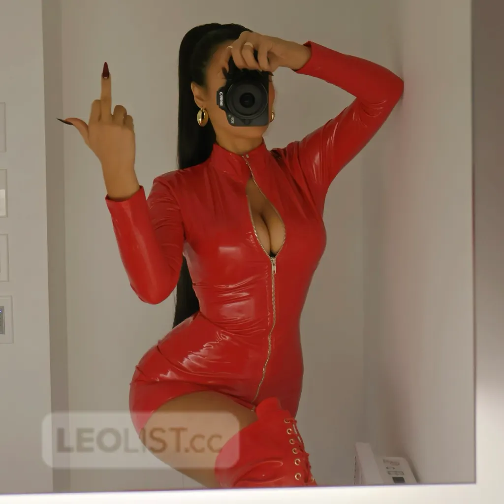 Mistress Valentina in a red latex dress taking a mirror selfie